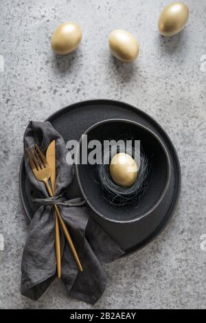 Easter table setting with black and golden decor on grey stone table. Top view. Vertical format. Minimal composition with nest. Stock Photo