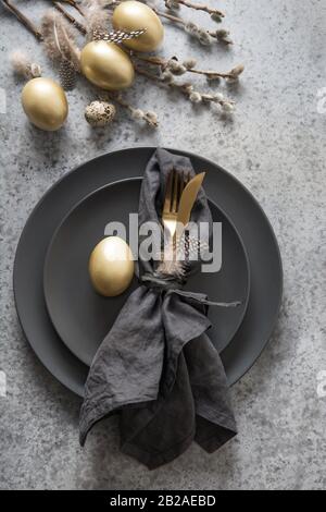 Easter table setting with black and golden decor on grey stone table. Top view. Vertical format. Stock Photo