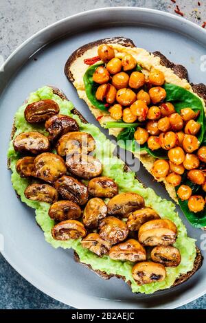 Open toasts with guacamole and mushrooms, hummus with chickpeas on rye bread. Healthy vegan food concept. Stock Photo