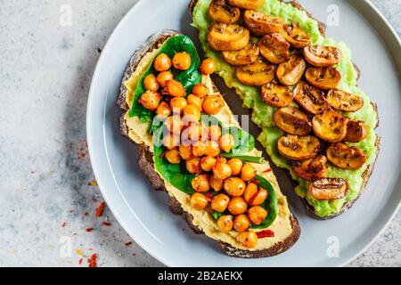 Open toasts with guacamole and mushrooms, hummus with chickpeas on rye bread. Healthy vegan food concept. Stock Photo