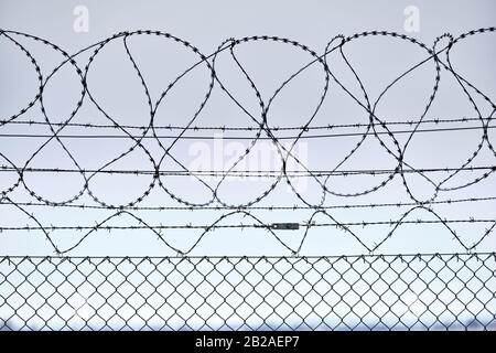 Close-up of a high chain-link fence with razor-barbed wire at the top protecting an airport in Germany Stock Photo