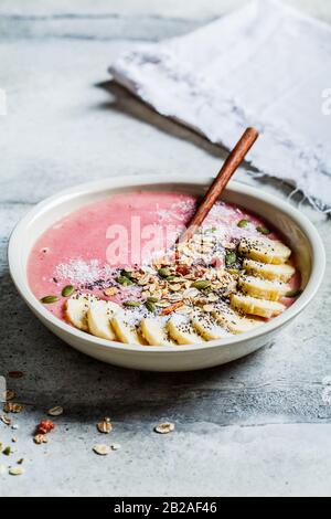 Acai smoothie bowl with granola, fruits and seeds in a white plate, gray background. Healthy vegan food concept. Stock Photo