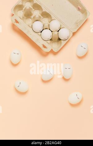 Happy Easter. White eggs with painted eyes in paper packaging on yellow background. Flat lay, top view, copy space. Stock Photo