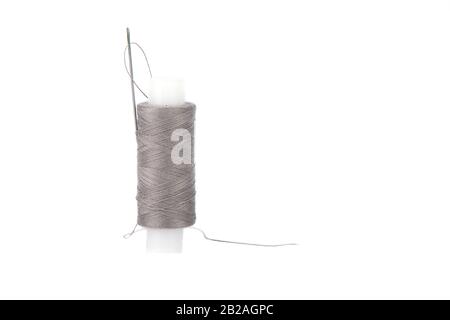 Close-up photo of a spool with grey thread and a needle isolated over white background. Thread in a sewing needle. Copy space. Stock Photo
