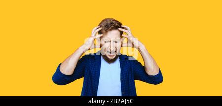 Caucasian man with beard is gesturing and showing his anger while touching his head and posing on a yellow background Stock Photo