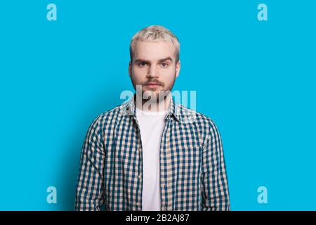 Caucasian man with blonde hair and beard is looking confidently at camera while posing on a blue wall Stock Photo