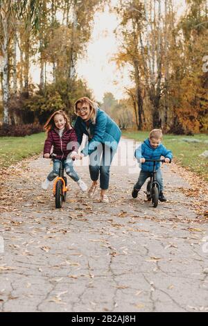 Careful caucasian mother is having fun with her kids riding the bikes in the park Stock Photo