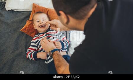 Playful caucasian father is tickling his small son who lying on the sofa and smile joyfully Stock Photo