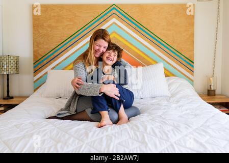 Mother and son sitting on a bed cuddling Stock Photo