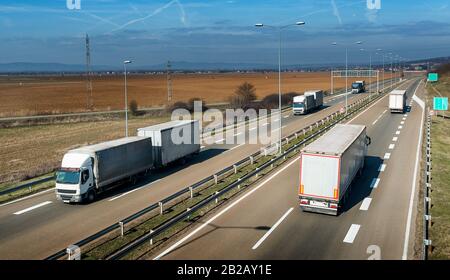 Convoy of transportation trucks passing on a highway on a bright blue ...