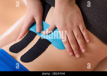 Physical therapist applying kinesio tape on female patient's lower back. Kinesiology, physical therapy, rehabilitation concept. Cropped shot close up. Stock Photo