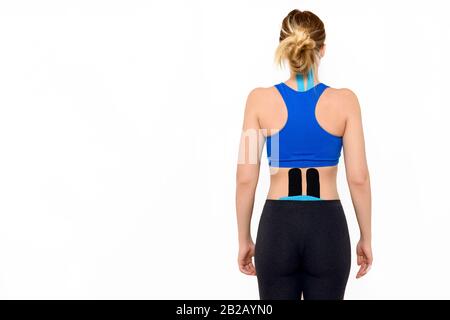 Rear view three quarter length studio shot of a female patient with kinesio tape on her neck and lower back, isolated over white background. Stock Photo