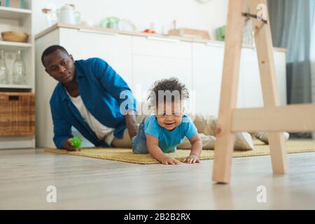 Portrait of cute African-American toddler crawling on carpet while playing with dad at home, copy space