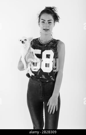 Studio shot of happy teenage girl smiling while standing and holding cute dog against white background Stock Photo