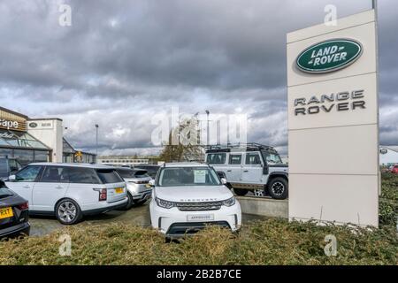 A Land Rover Discovery, with Defender in background, on forecourt of Land Rover Range Rover dealership. Stock Photo