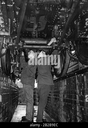 An engineer and a fireman controlling the brake mechanism under the engine (undated picture). Stock Photo