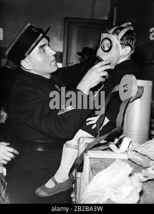 Mobilization in France during the last weeks of peace before the Second World War. Gas masks, that the French government had previously received from Czechoslovakia after the Sudeten crisis of September 1938, are distributed in six Parisian arrondissements.  The arrondissements were chosen at random. In the picture a soldier puts a gas mask on a little boy in a distribution station. Stock Photo