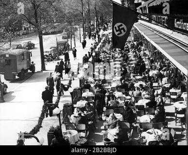Guests sit on the street in Cafe Kranzler on the Kurfuerstendamm in Berlin. A swastika flag is hanging from above. Stock Photo