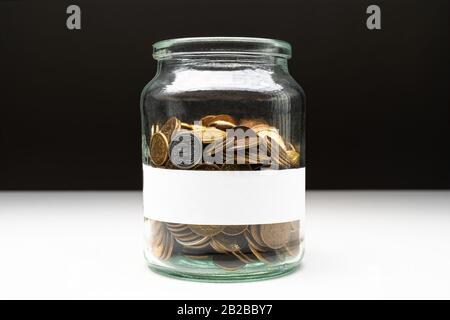 Coins in a jar with blank white label. Savings abstract concept. Copy space. Stock Photo