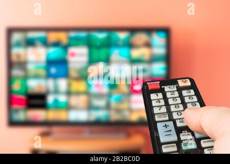 Caucasian man choosing what to watch on TV at home. Video on demand or VOD abstract concept. Changing channels with television remote. Stock Photo