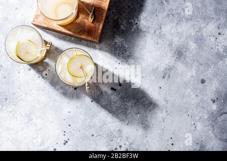 Cold pear cocktail mocktail with soda and pear puree and fruit slices in short glass on gray background with shadow.Refreshing summer drink with ice Stock Photo