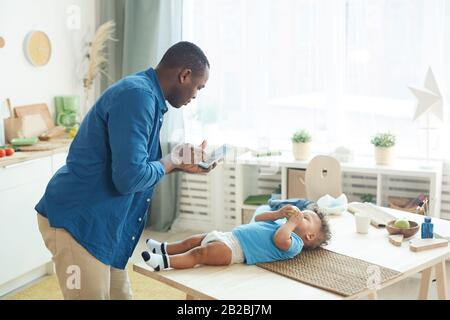 Side view portrait of mature African man calling wife while caring for baby in home interior, copy space Stock Photo