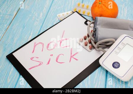 Medical pills against hypertension, equipment for measuring blood pressure in the background, the inscription on the sheet not sick. Stock Photo