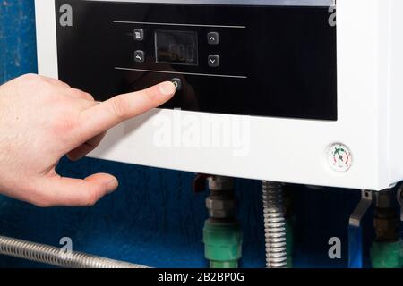 The man's finger turns on or off the start button of the heating system in the boiler room. The concept of home heating in the autumn-winter season Stock Photo