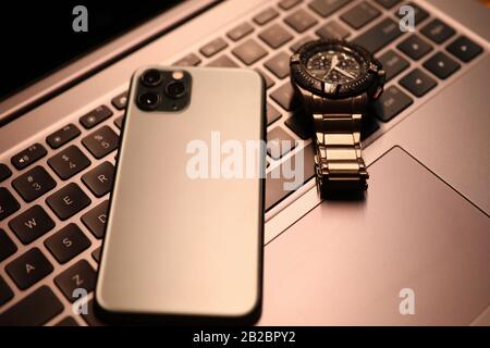 Silver smartphone and watch lie on laptop keyboard in office close-up Stock Photo