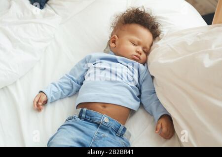 Top view at cute mixed-race baby sleeping on comfortable bed in white sheets Stock Photo