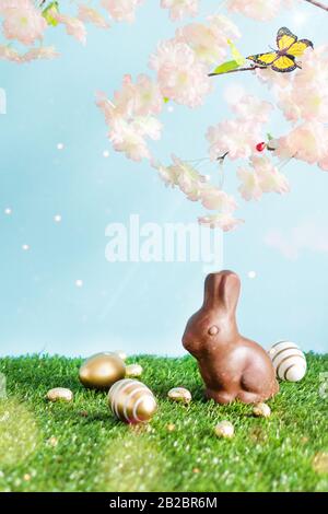 Easter colored eggs, chocolate Easter bunny and blooming spring tree branches over blue background. Happy Easter time. Easter greeting card background Stock Photo