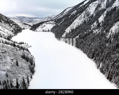 Aerial view of Kolsay mountain lake and forest at winter time in the mountains of Kazakhstan. Drone shot, top view. Stock Photo