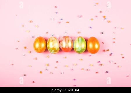 Five colored Easter eggs lie on a pink background among the gypsophila flowers. Stock Photo