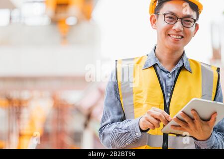Image outside the industrial construction engineers in yellow protective helmet discuss new project while using laptop and happy smile on the open bui Stock Photo