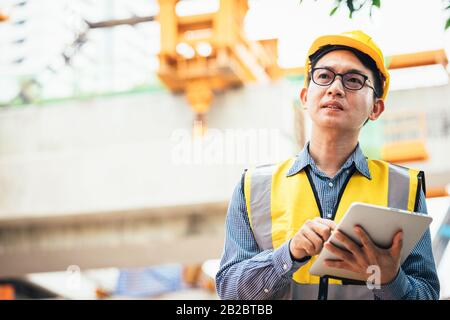 Image outside the industrial construction engineers in yellow protective helmet discuss new project while using laptop and happy smile on the open bui Stock Photo