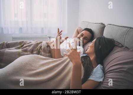 Young happy couple is lying in bed in the morning and talking. Stock Photo