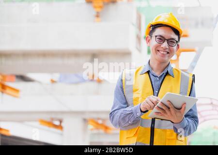Image outside the industrial construction engineers in yellow protective helmet discuss new project while using laptop and happy smile on the open bui Stock Photo