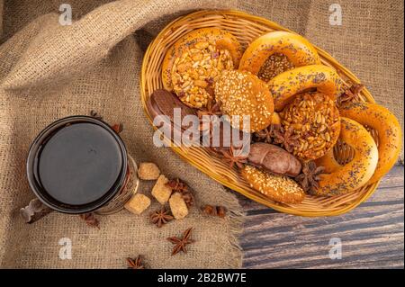 Cookies, chocolate cakes, bagels in a wicker basket and a glass of tea in a vintage Cup holder against a background of rough homespun fabric. Close up Stock Photo