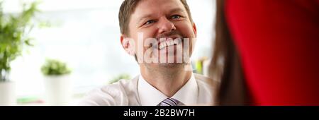 Young smiling businessman sitting and making agreement by handshake with colleague Stock Photo