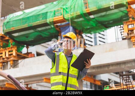 Image outside the industrial construction engineers in yellow protective helmet discuss new project while walkie talkie and happy smile on the open bu Stock Photo