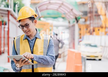 Image outside the industrial construction engineers in yellow protective helmet discuss new project while using laptop and happy smile on the open bui Stock Photo
