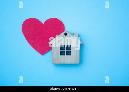 Love home, insurance and mortgage, marriage and valentine concept. Small wooden house toy and paper heart shape on blue background top view Stock Photo