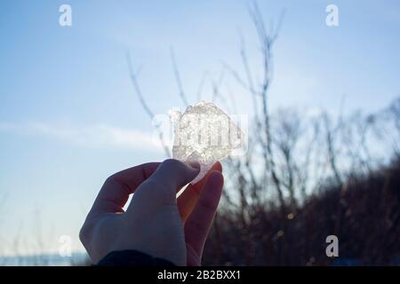 Piece of ice in man's hand close up against the sun. Look at the sun through the ice Stock Photo