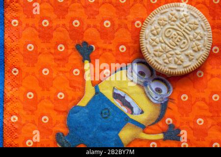 Golden Oreo biscuits on serviette with Minions - Minion juggling with Golden Oreo biscuit, sandwich biscuits with a vanilla flavour filling Stock Photo