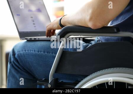 Man sitting in wheelchair working with laptop computer Stock Photo