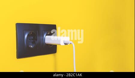 Doubled black socket on yellow wall. White fork sticks out of one of the socketes. Electricity concept. Copy space. Stock Photo