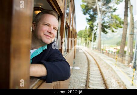 Man traveling by retro wooden train, looking through the window. Beautiful landscape of mountains. Majorca, Spain. Stock Photo