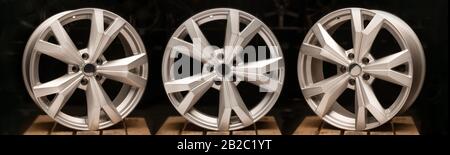 three silvery new cast aluminum wheels on a black background close-up, long layout. Stock Photo