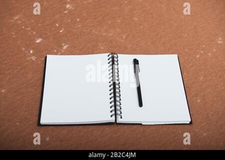 open notebook to point with a pen on a brown background Stock Photo
