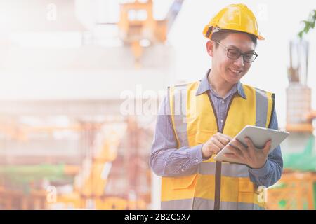 Image outside the industrial construction engineers in yellow protective helmet discuss new project while using laptop and happy smile on the open bui Stock Photo